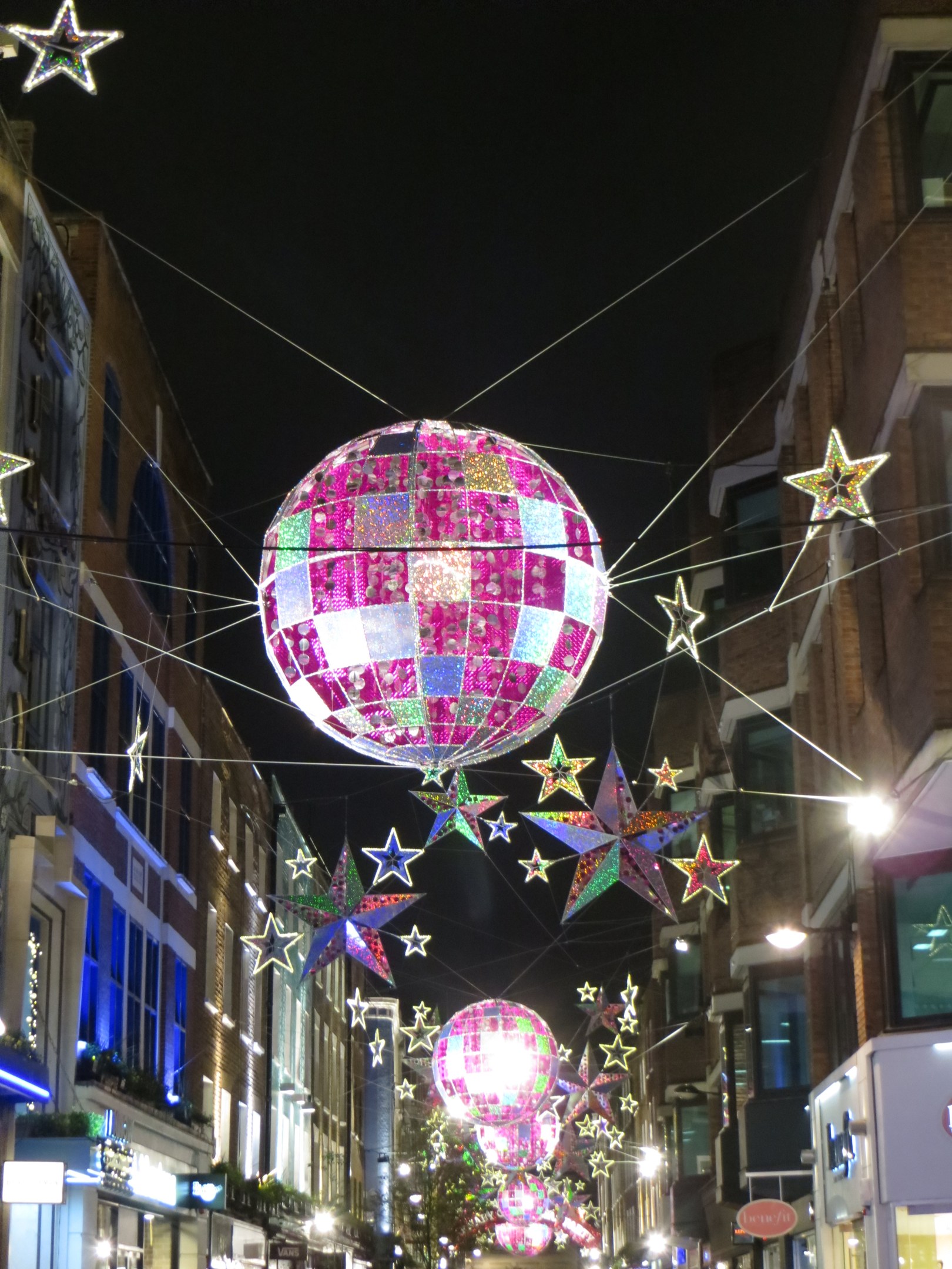 Eine stra├če voller Lichter und eine gro├če Diskokugel, die von einem Geb├Ąude h├Ąngt, erstellt eine festliche Atmosph├Ąre gegen einen dunklen Himmel.