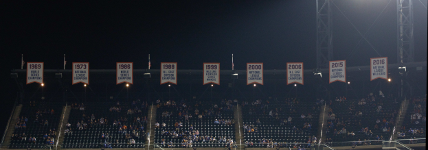 Baseballstadion voller Zuschauer auf Tribüne unter hellen Scheinwerfern, mit Bannern im Hintergrund vor dunklem Himmel.