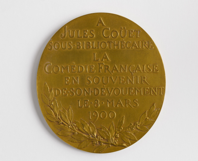 Goldmedaille mit einem Lorbeerkranz und der Inschrift "A Jules Couet Sous Bibliothèque" vor einem weißen Hintergrund.