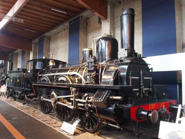 Alte Dampflokomotive in einem Museums Setting mit Eisenbahnschienen, Informationsschildern und Beleuchtung im Hintergrund.