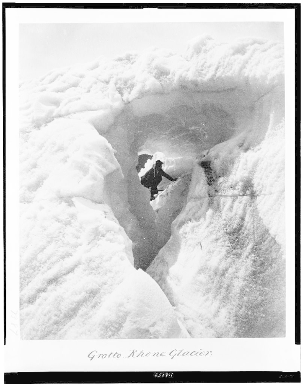 Schwarz-weißes Foto einer Person, die eine schneebedeckte Bergwand hochklettert, mit der Beschriftung "Grotto Rhone Glacier", umgeben von schneebedeckter Landschaft und Himmel im Hintergrund.
