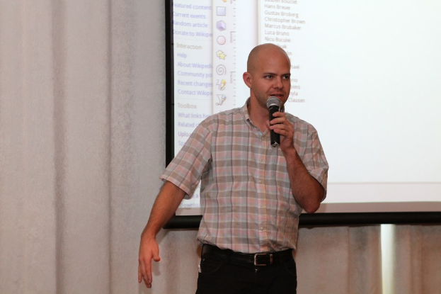 Eine Person steht mit einem Mikrofon vor einer Projektionsfläche.