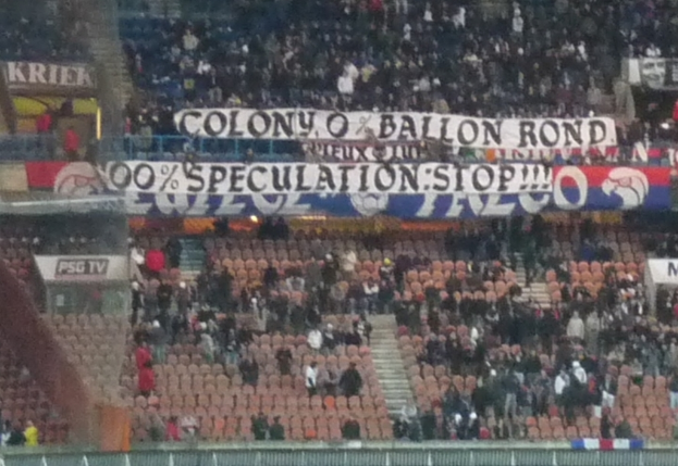 Ein Stadion voller Menschenmenge, Banner und Stühle, mit einem Zaun unten und einer Treppe links.