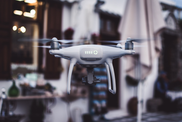 Weißer DJI Phantom 3 Advanced Drohne fliegt gegen einen unscharfen Hintergrund von Gebäuden und Lichtern.