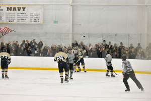 Eine Gruppe von Menschen, die Eishockey auf einer Eisfläche spielen, tragen Helme und halten Eishockeystöcke, mit Zuschauern auf den Tribünen und einem Banner an der Wand im Hintergrund.