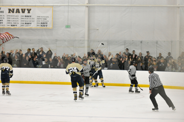 Eine Gruppe von Menschen, die Eishockey auf einer Eisfläche spielen, tragen Helme und halten Eishockeystöcke, mit Zuschauern auf den Tribünen und einem Banner an der Wand im Hintergrund.