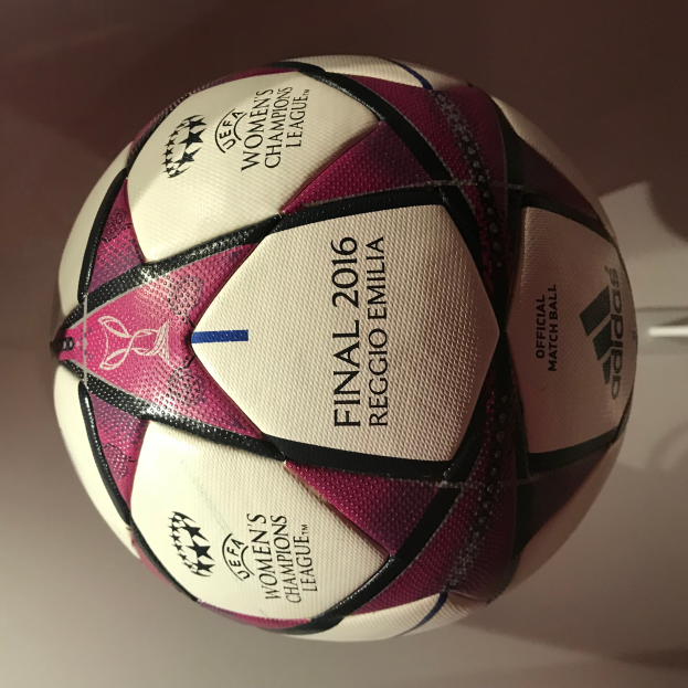 Ein Fußball auf einem weißen Tisch mit 'UEFA Women's Champions League Final 2016' geschrieben in Weiß, Rosa und Schwarz.