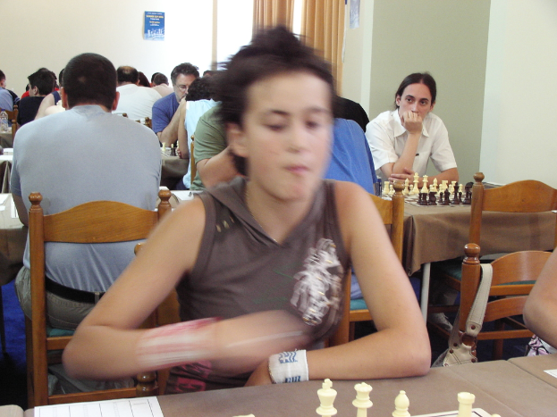 Ein Raum mit Menschen, die an Tischen Schach spielen, mit einer Vorhangwand und einem Foto in der Ecke.