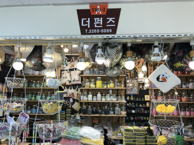 Ein unordentlicher Laden in Seoul mit verschiedenen Gegenständen wie Körben, Lampen, Flaschen und Spielzeugen auf Regalen, mit einer Tafel oben, die anzeigt, dass es einer der besten koreanischen Läden in Seoul ist.