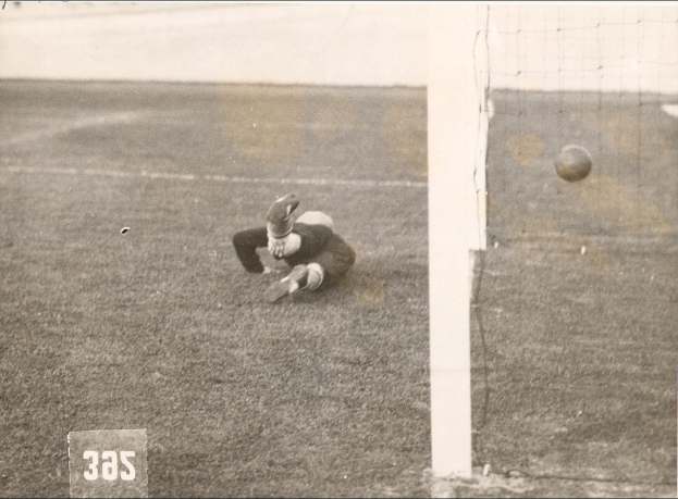 Ein Schwarz-Weiß-Foto eines Fußballspielers, der einen Ball vor einem Torpfosten mit Netz auf der rechten Seite fängt.