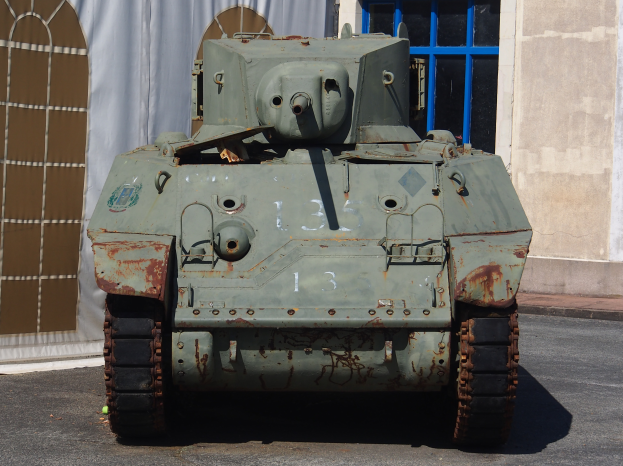 Ein alter Militärpanzer steht auf einer Straße vor einem Gebäude mit einem Fenster und einem Vorhang im Hintergrund und sieht bereit für die Aktion aus.