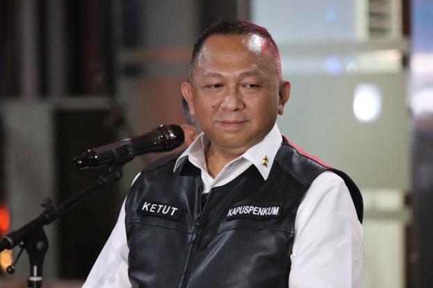 Ein Mann in einer schwarzen Weste und einem weißen Hemd steht vor einem Mikrofon und sieht besorgt aus, mit einem unscharfen Hintergrund.