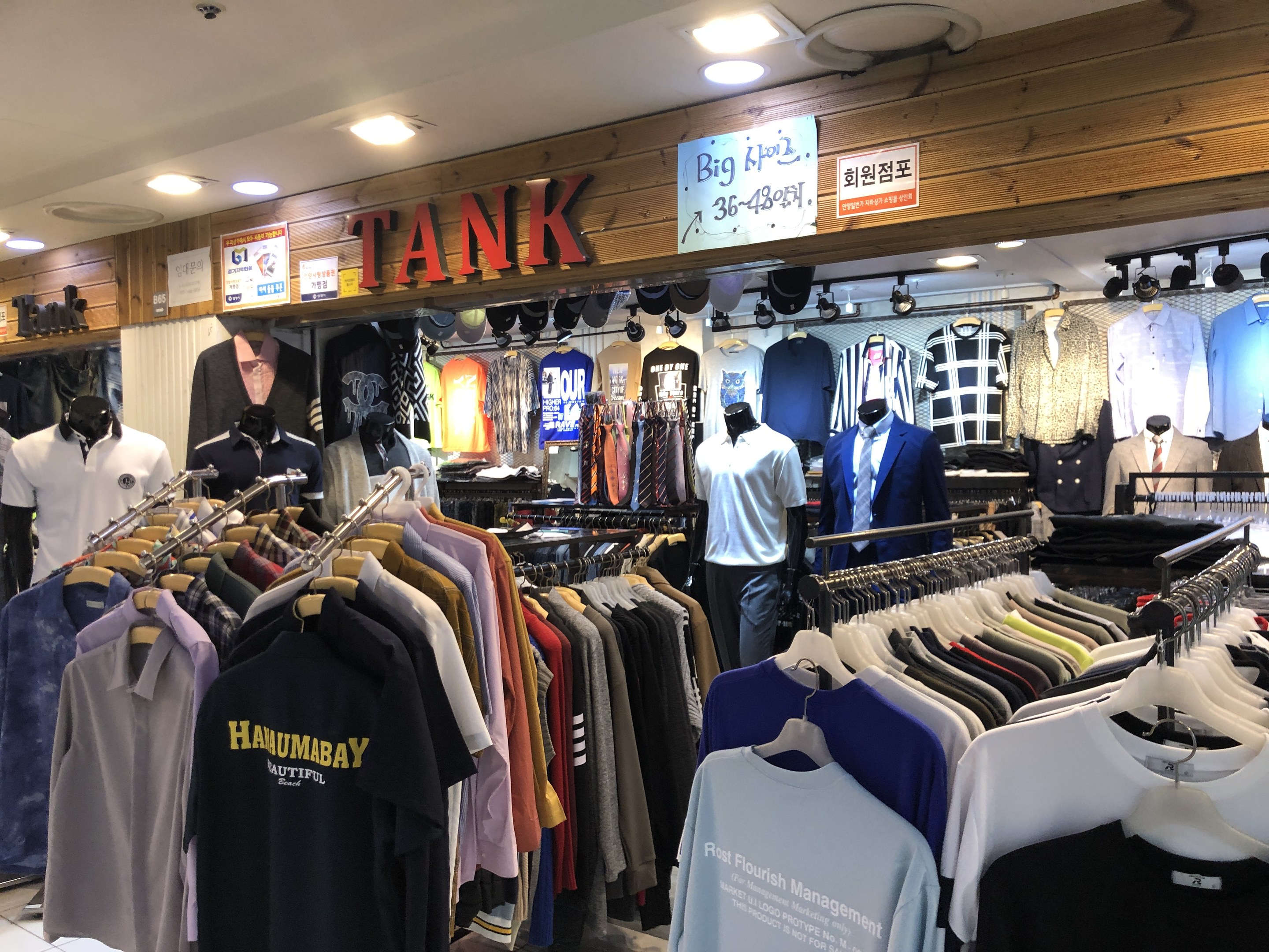 Ein moderner Bekleidungsladen mit zahlreichen Hemden auf der Auslage, Schaufensterpuppen, die die aktuelle Mode präsentieren, Texttafeln an den Wänden und Deckenleuchten.