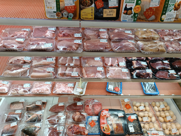 Eine Supermarkttheke voller verschiedener Fleischsorten in Plastikboxen, anderen Lebensmitteln und Preisschildern.