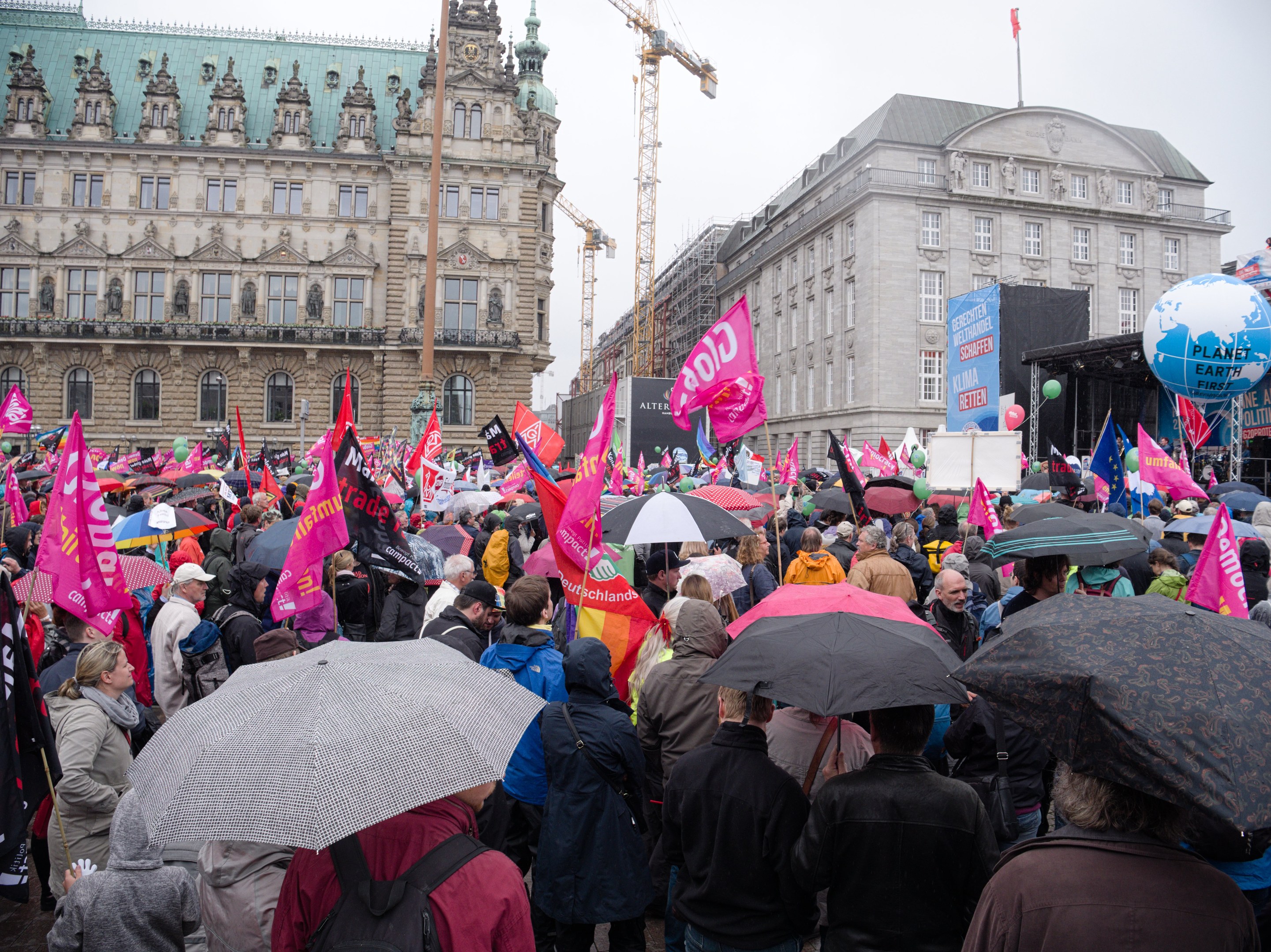 Eine große Gruppe von Menschen bei einer Frauen-Demo in Berlin, die vor einem Gebäude stehen und Schirme, Plakate und Luftballons halten.
