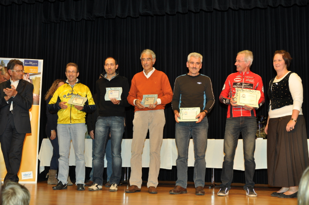 Eine Gruppe von Menschen auf einer Bühne mit Urkunden in den Händen, im Hintergrund eine Fahne, ein Tisch daneben und ein schwarzer Vorhang.