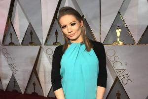 Frau in blauem und schwarzem Kleid auf einem roten Teppich bei den Oscars 2018 Red Carpet Arrivals, mit Text und abstrakten Skulpturen im Hintergrund.