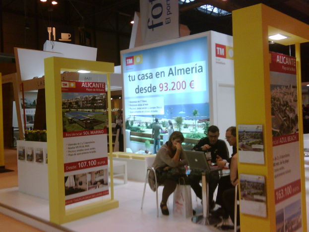 Eine Gruppe von Menschen, die in Stühlen sitzen und einem Tisch mit einem Laptop gegenüberstehen, umgeben von mehreren Flyern mit verschiedenen Anzeigen.