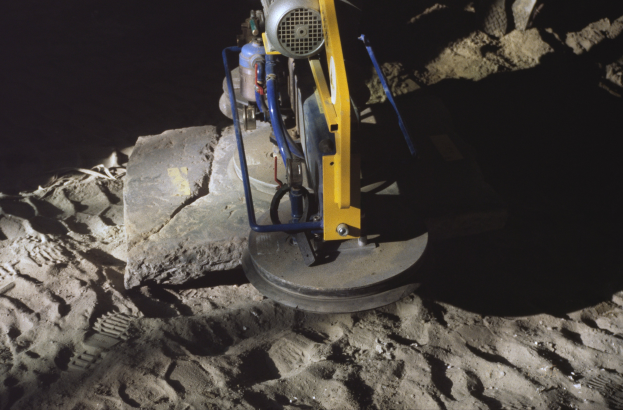 Eine Bodenpoliermaschine ist auf einem Schmutzfeld mit einem Felsen im Hintergrund positioniert.