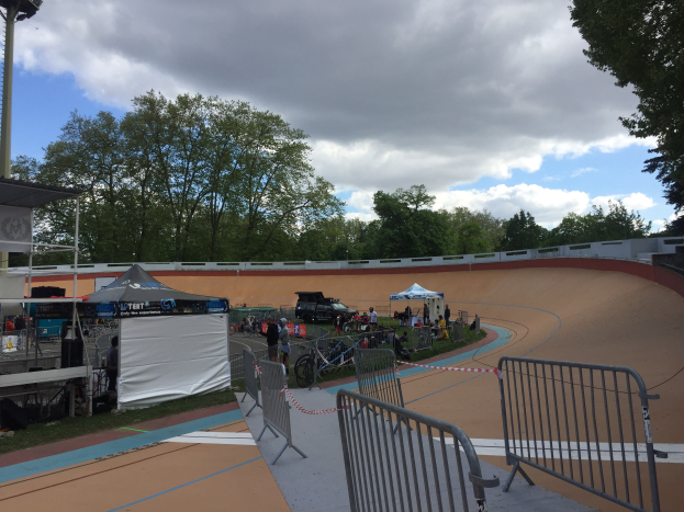 Eine Gruppe von Radfahrern, die auf einer BMX-Piste aus Erde bei den UCI-BMX-Weltmeisterschaften 2018 fahren, mit Zelten, Fahrzeugen und Bäumen im Hintergrund.