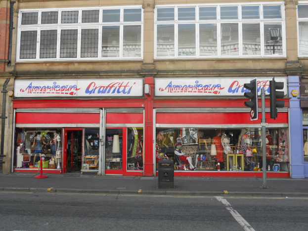 Eine Straßenszene mit einem Gebäude, mehreren Schaufensterpuppen, einem M├╝llcontainer, einem Pfahl, Verkehrsampeln und einer Brille auf dem Boden.