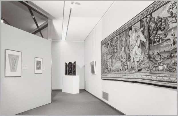 Schwarz-weiß-Foto einer Museumsgalerie mit einem großen Wandteppich, gerahmten Kunstwerken an den Wänden, Sockeldisplays und Deckenleuchten, beschriftet mit "Museum of Fine Arts, New York City" unten.