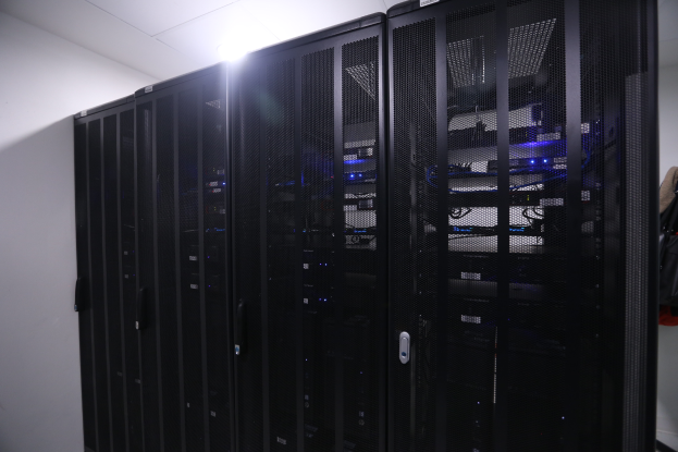 Eine Reihe von Servern in einem Datenzentrum, ordentlich mit einer Wand im Hintergrund und einer Lampe oben.