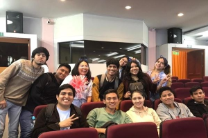 Gruppe von Menschen, die fröhlich in einem Kino posieren, mit Lautsprechern an der Wand und Deckenbeleuchtung, wahrscheinlich auf einem Filmfestival.