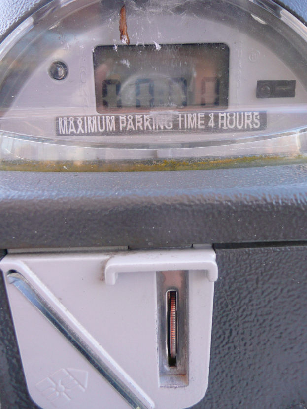 Ein Parkautomat mit der Anzeige "Maximale Parkzeit 4 Stunden" und einem Münzschlitz mit einer Münze.