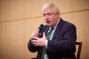 Ein Mann im Anzug und Krawatte sitzt in einem Stuhl und hält ein Mikrofon, während er in eine hitzige Diskussion vertieft zu sein scheint.