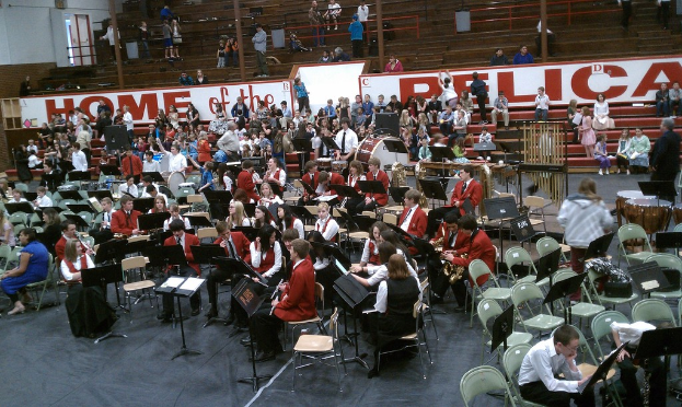 Eine Gruppe von Kindern sitzt auf Stühlen in einem Stadion während einer Musikstunde, mit Stadion-Sitzen im Hintergrund.