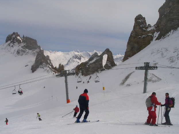 Menschen in Pullovern fahren mit einer Seilbahn auf den Ski, Berge und einen bewölkten Himmel im Hintergrund.