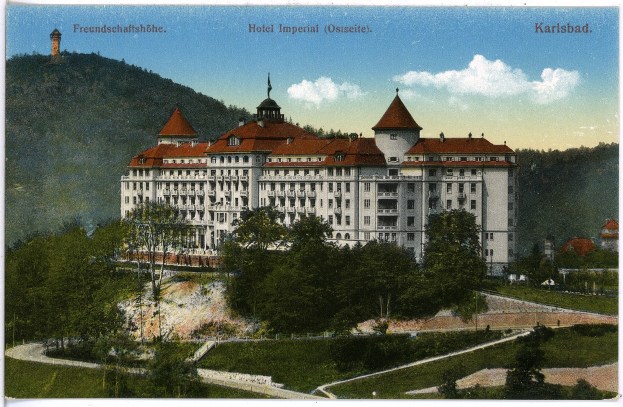 Alte Postkarte des Hotels Imperial in Karlsbad, Deutschland, zeigt ein großes Gebäude mit Fenstern, umgeben von Bäumen, Pflanzen, Gras, einem Pfad, einer Baumgruppe, Hügeln und einem bewölkten Himmel, mit Text oben.