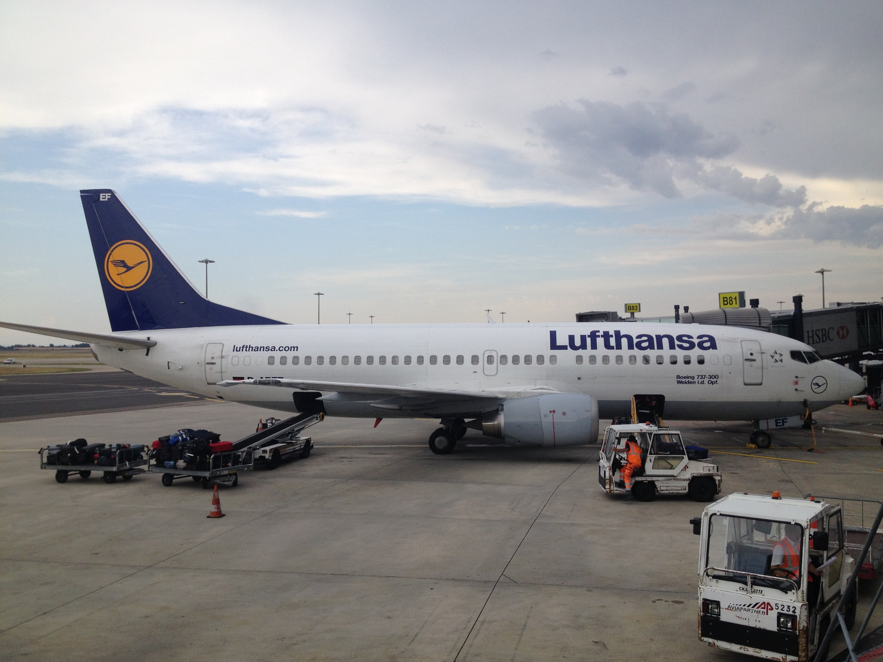 Lufthansa Airbus A320-200 auf dem Frankfurter Flughafen geparkt mit Bodenfahrzeugen, Verkehrskegeln und Informationsschildern im Hintergrund unter einem bewölkten Himmel.
