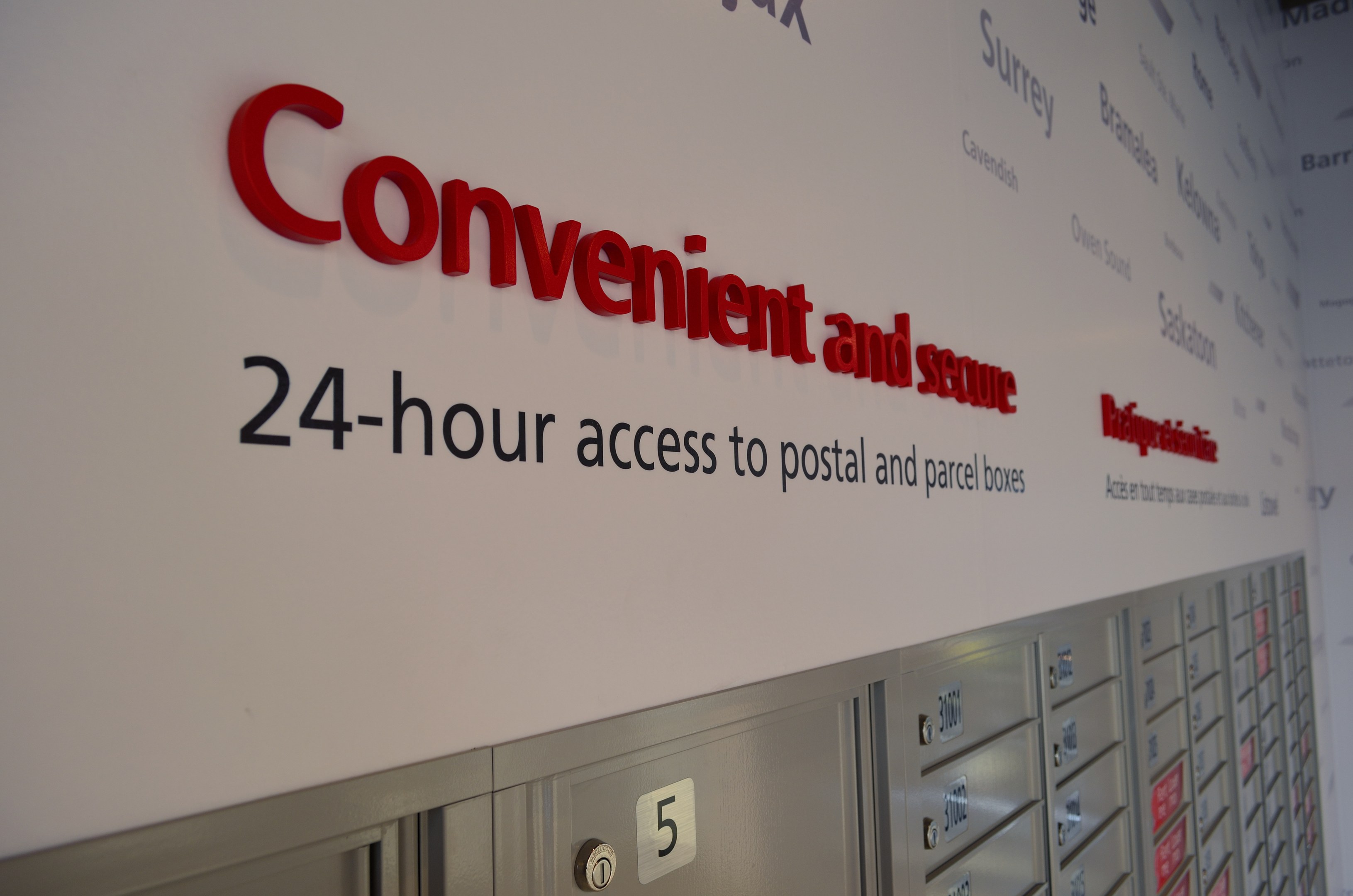 Ein Wandschild mit der Aufschrift "bequem und sicher 24-Stunden-Zugang zu Brief- und Paketfächern" über nummerierten Fächern.