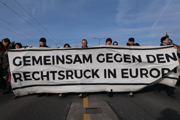 Gruppe von Menschen mit einem Banner "Gemeinsam gegen den Rechtsruck in Europa" bei einer Protestaktion gegen die Europäische Union, mit Straßeninfrastruktur und Gebäuden im Hintergrund.