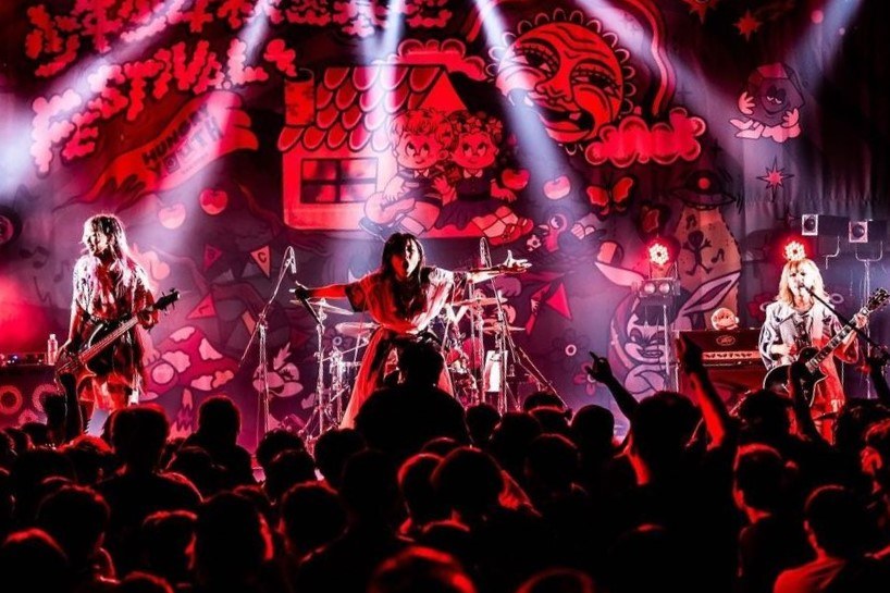 Ein Live-Auftritt der japanischen Rockband Korn auf der Bühne, mit Bandmitgliedern, die Gitarren spielen und in Mikrofone singen, während das Publikum darunter zusieht.