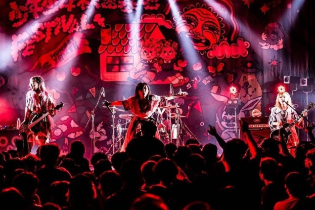 Ein Live-Auftritt der japanischen Rockband Korn auf der Bühne, mit Bandmitgliedern, die Gitarren spielen und in Mikrofone singen, während das Publikum darunter zusieht.