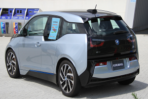 Ein BMW i3 Elektroauto vor einem Gebäude geparkt, mit einer Pflanze im Vordergrund und einer Wand im Hintergrund, das ein zentral positioniertes Rad zeigt.