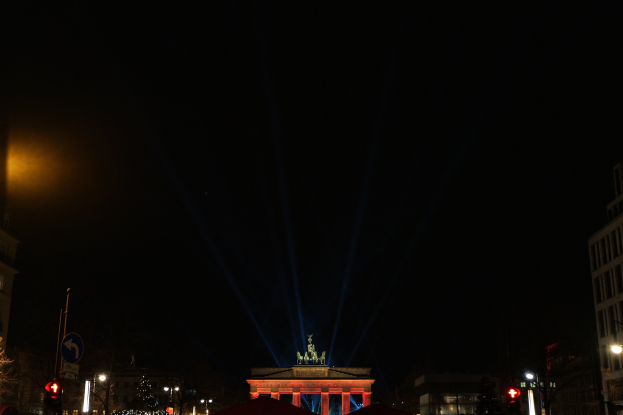 Das Brandenburger Tor in Berlin nachts, von Straßenlaternen beleuchtet, mit umliegenden Gebäuden, Bäumen, Pfählen, Verkehrszeichen, Schildern und Zelten gegen einen dunklen Himmel.